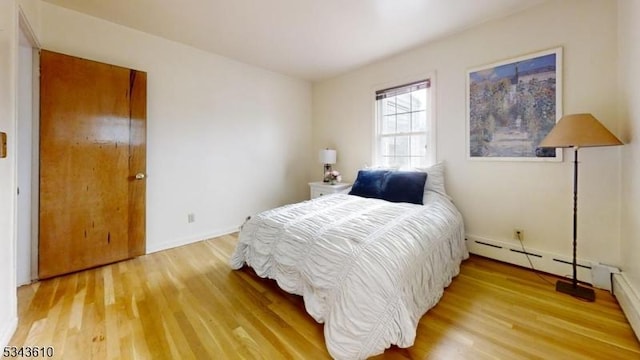 bedroom with light wood finished floors and a baseboard heating unit