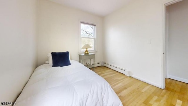 bedroom with a baseboard heating unit, light wood-style floors, and baseboards