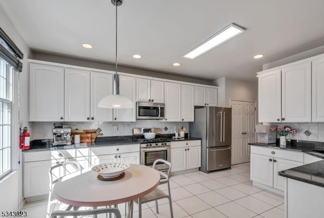 kitchen with light tile patterned floors, white cabinets, appliances with stainless steel finishes, dark countertops, and tasteful backsplash