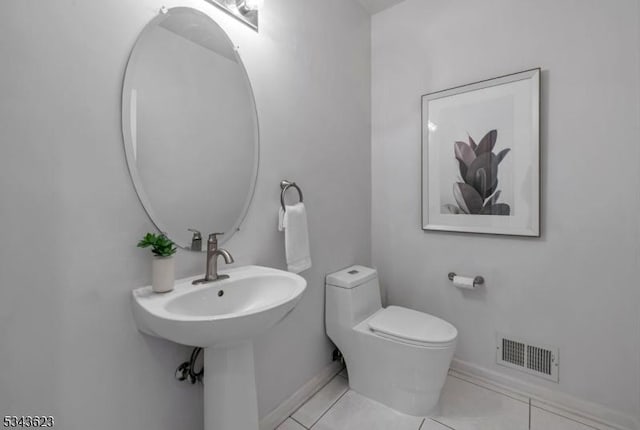 half bathroom featuring visible vents, baseboards, toilet, tile patterned floors, and a sink