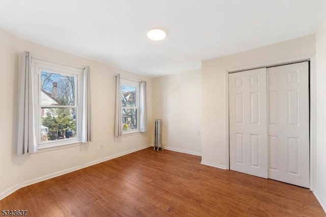 unfurnished bedroom featuring a closet, baseboards, wood finished floors, and radiator heating unit