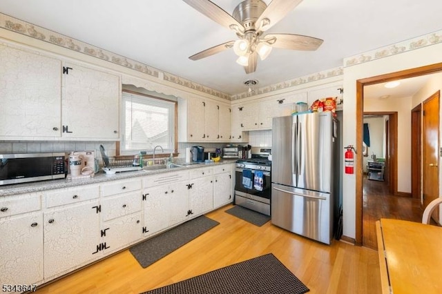 kitchen with light wood-type flooring, a sink, stainless steel appliances, white cabinets, and light countertops