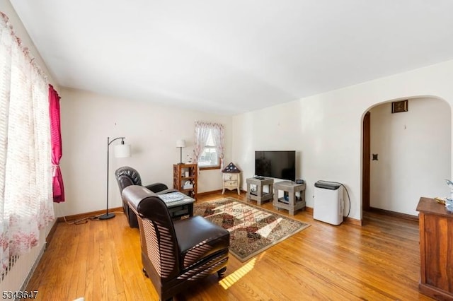 living room with baseboards, arched walkways, and light wood finished floors