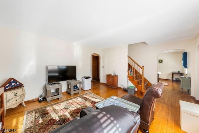 living area featuring stairs, wood finished floors, and arched walkways