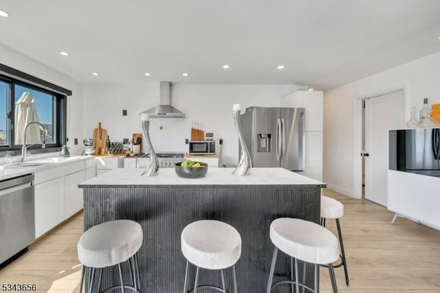 kitchen with a sink, wall chimney range hood, white cabinetry, appliances with stainless steel finishes, and light wood finished floors