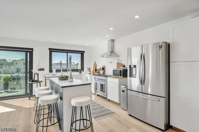 kitchen with a kitchen island, wall chimney range hood, stainless steel appliances, light wood-style floors, and white cabinetry