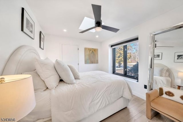 bedroom with light wood-type flooring, a ceiling fan, recessed lighting, a skylight, and baseboards