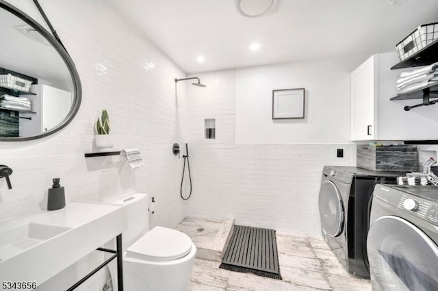 bathroom featuring toilet, a tile shower, recessed lighting, separate washer and dryer, and tile walls