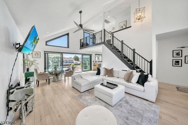 living room featuring ceiling fan with notable chandelier, stairway, wood finished floors, and high vaulted ceiling