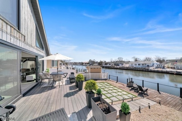 wooden terrace featuring outdoor dining space, fence, and a water view