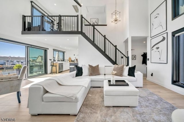 living room featuring wood finished floors, baseboards, stairs, a towering ceiling, and a notable chandelier