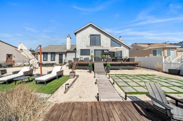 rear view of property with a wooden deck, a chimney, and fence