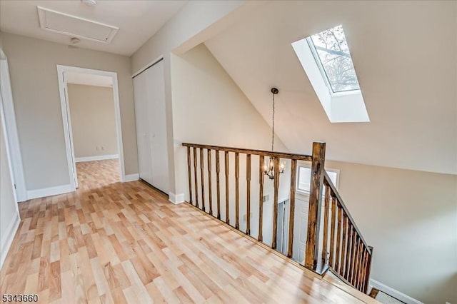 hallway featuring an upstairs landing, vaulted ceiling with skylight, baseboards, and wood finished floors