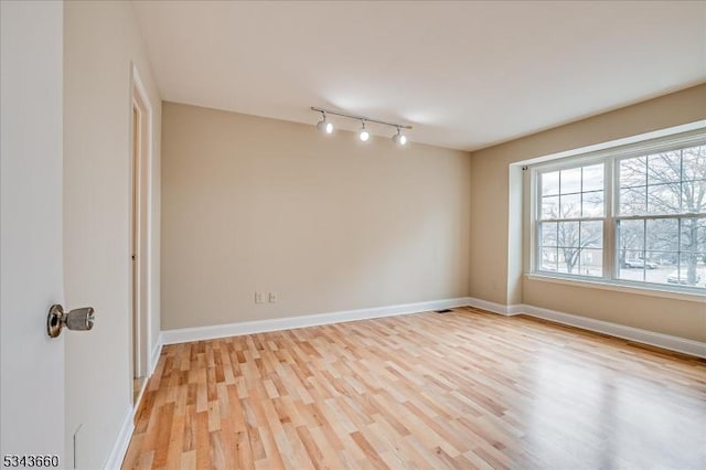 empty room featuring baseboards, light wood-style flooring, and track lighting