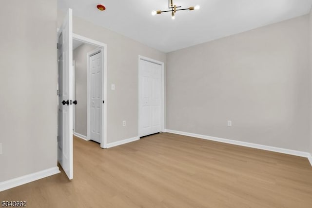 unfurnished bedroom featuring a closet, a notable chandelier, light wood-type flooring, and baseboards