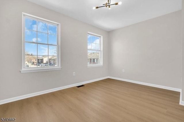 unfurnished room featuring visible vents, baseboards, wood finished floors, and a chandelier