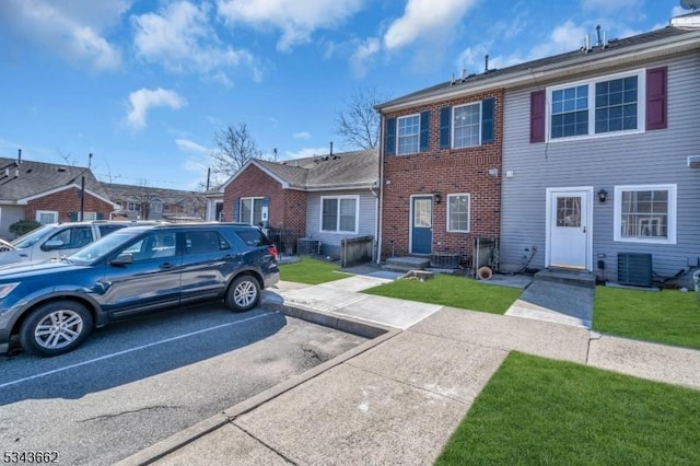 view of front facade featuring a front yard, central AC unit, uncovered parking, entry steps, and brick siding