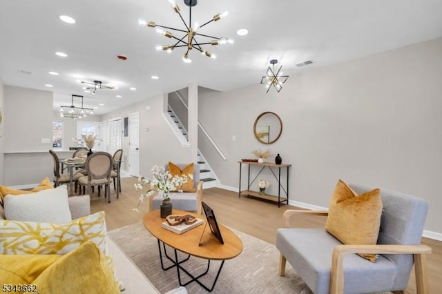 living room featuring visible vents, light wood-type flooring, stairs, and an inviting chandelier