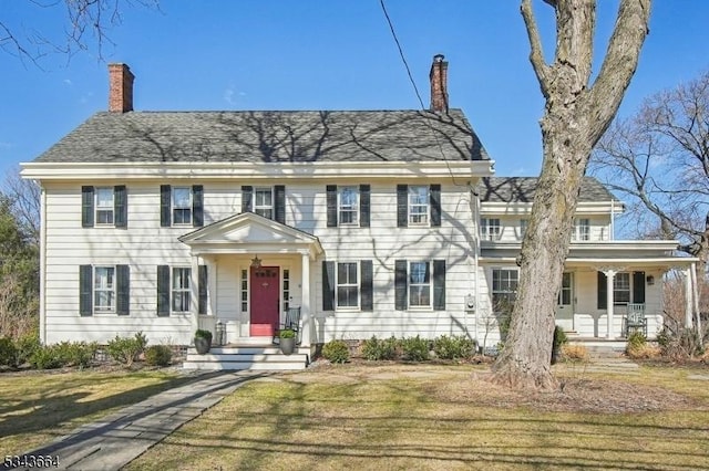 colonial house with a shingled roof, a front yard, a porch, and a chimney