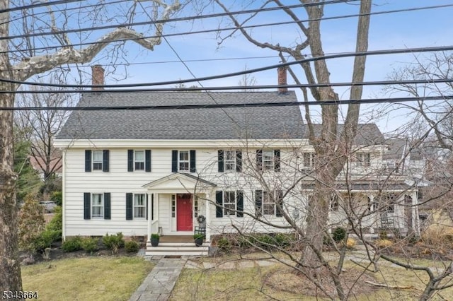 colonial inspired home featuring a front yard, roof with shingles, and a chimney