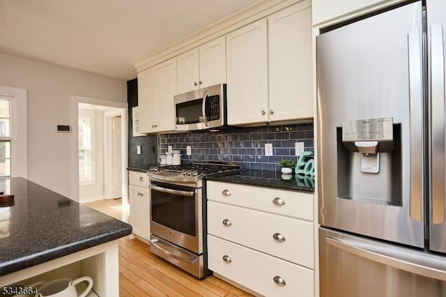 kitchen with backsplash, light wood-type flooring, dark stone countertops, stainless steel appliances, and white cabinetry