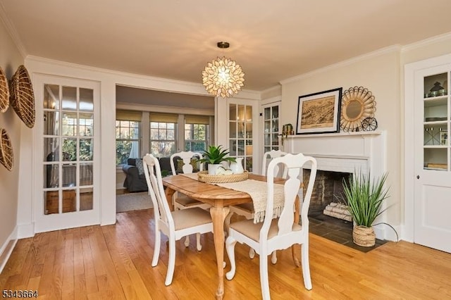 dining room featuring a fireplace with flush hearth, an inviting chandelier, crown molding, and light wood finished floors