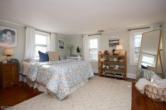 bedroom with radiator heating unit, wood finished floors, baseboards, and ornamental molding