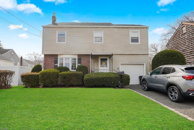 colonial home with a front yard, driveway, a chimney, a garage, and brick siding