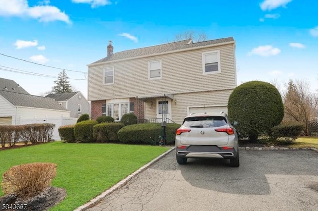 colonial house with aphalt driveway, a front lawn, a chimney, and an attached garage