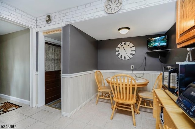 dining space with light tile patterned floors and a wainscoted wall