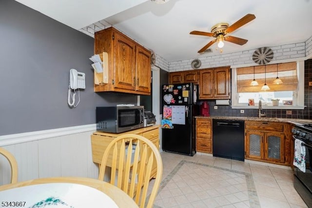 kitchen with black appliances, light tile patterned flooring, brown cabinetry, wainscoting, and ceiling fan