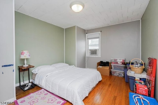 bedroom with cooling unit, baseboards, and wood finished floors