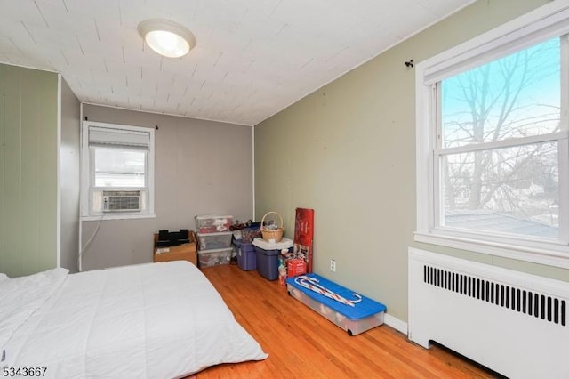 bedroom with multiple windows, radiator heating unit, wood finished floors, and cooling unit