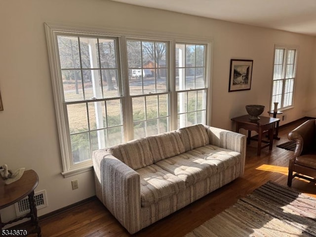 living area with a wealth of natural light, visible vents, baseboards, and dark wood-style floors