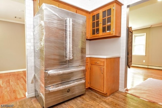 kitchen with light wood finished floors, a baseboard heating unit, crown molding, glass insert cabinets, and light countertops