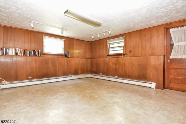 empty room featuring tile patterned floors, baseboard heating, wood walls, and track lighting