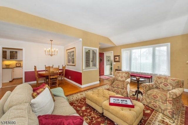 living area featuring ornamental molding, wood finished floors, baseboards, a chandelier, and vaulted ceiling