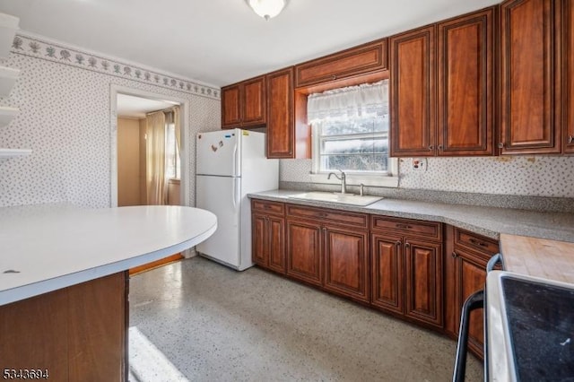 kitchen featuring wallpapered walls, freestanding refrigerator, a sink, light countertops, and range