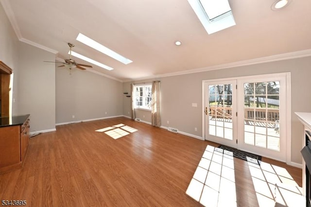 unfurnished living room featuring visible vents, lofted ceiling with skylight, light wood-style flooring, crown molding, and baseboards