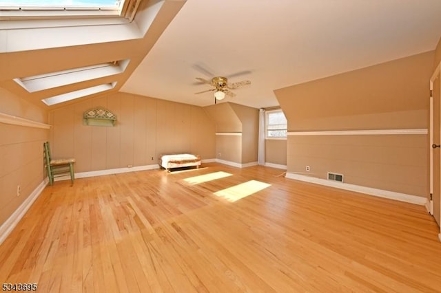 bonus room with visible vents, a ceiling fan, vaulted ceiling with skylight, light wood-style floors, and baseboards