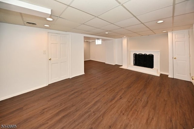 finished below grade area featuring a drop ceiling, baseboards, dark wood-type flooring, and a fireplace with raised hearth