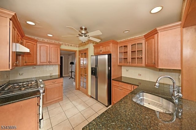 kitchen with dark stone countertops, light tile patterned floors, a sink, under cabinet range hood, and appliances with stainless steel finishes