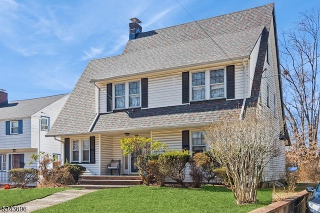 view of front of home with a porch, a chimney, a front lawn, and a shingled roof