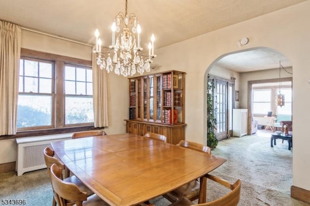 carpeted dining space with arched walkways, radiator, and an inviting chandelier