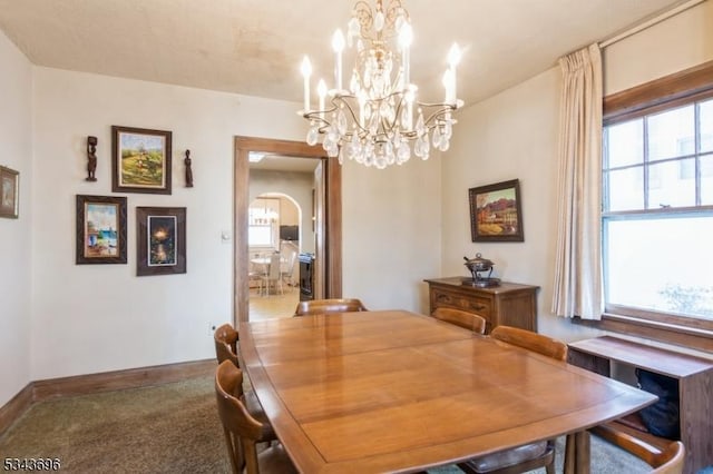 carpeted dining room featuring an inviting chandelier, baseboards, and arched walkways