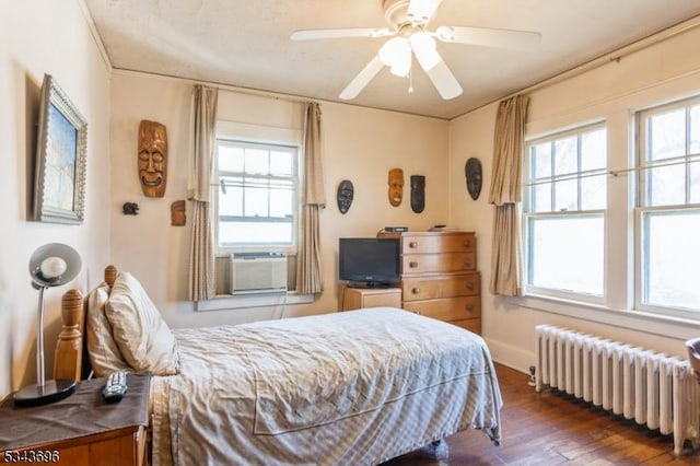 bedroom featuring ceiling fan, multiple windows, wood-type flooring, and radiator heating unit