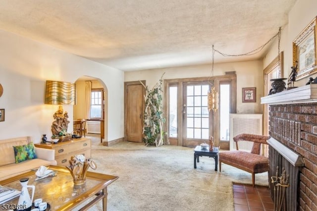 carpeted living area featuring arched walkways, a textured ceiling, and a brick fireplace