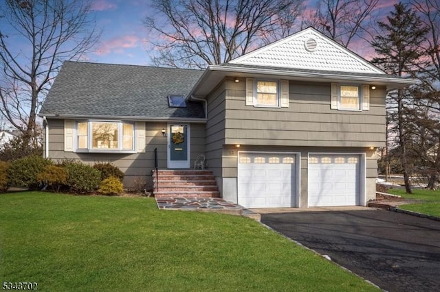 tri-level home featuring aphalt driveway, a garage, roof with shingles, and a front yard