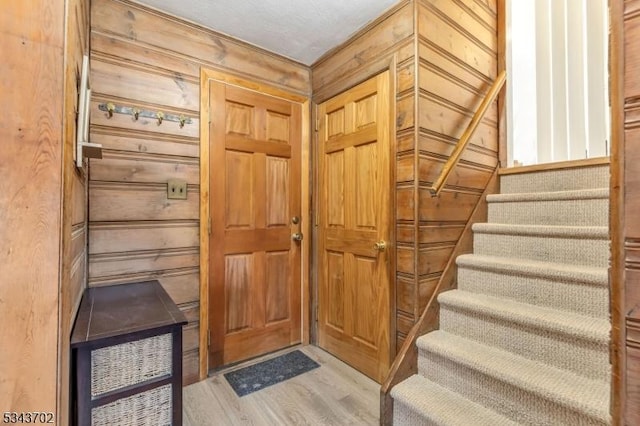 entryway with stairs, wood finished floors, and wood walls