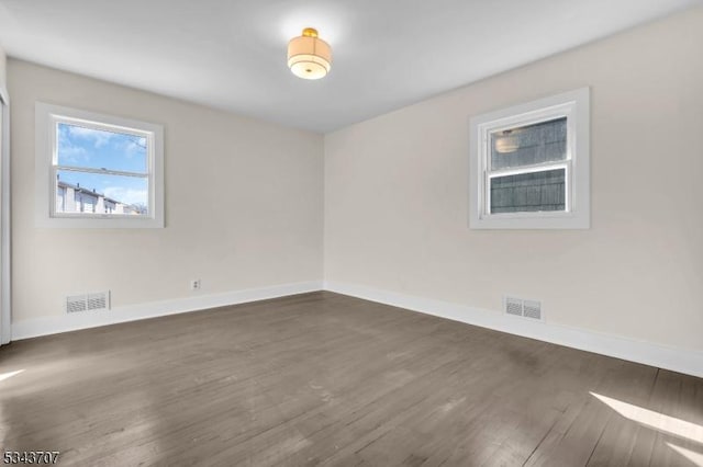 empty room featuring visible vents, baseboards, and dark wood-style flooring